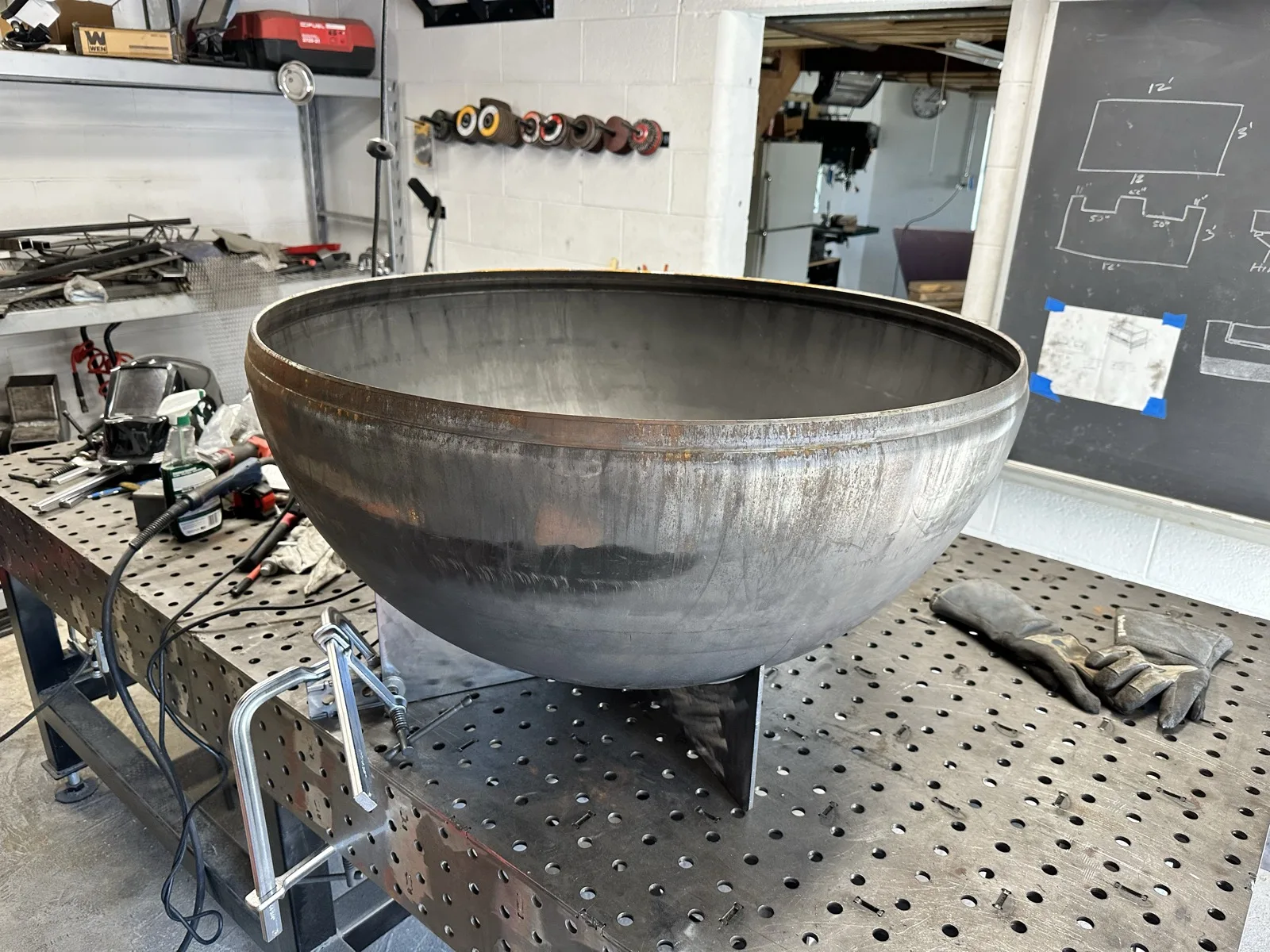 Large welded steel bowl resting on a welding table